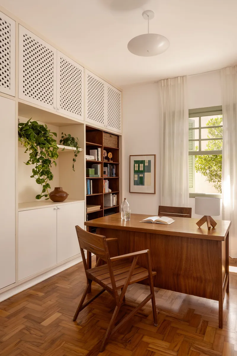 Home office with walnut desk, perforated upper cabinets, herringbone wood floor and potted trailing plants