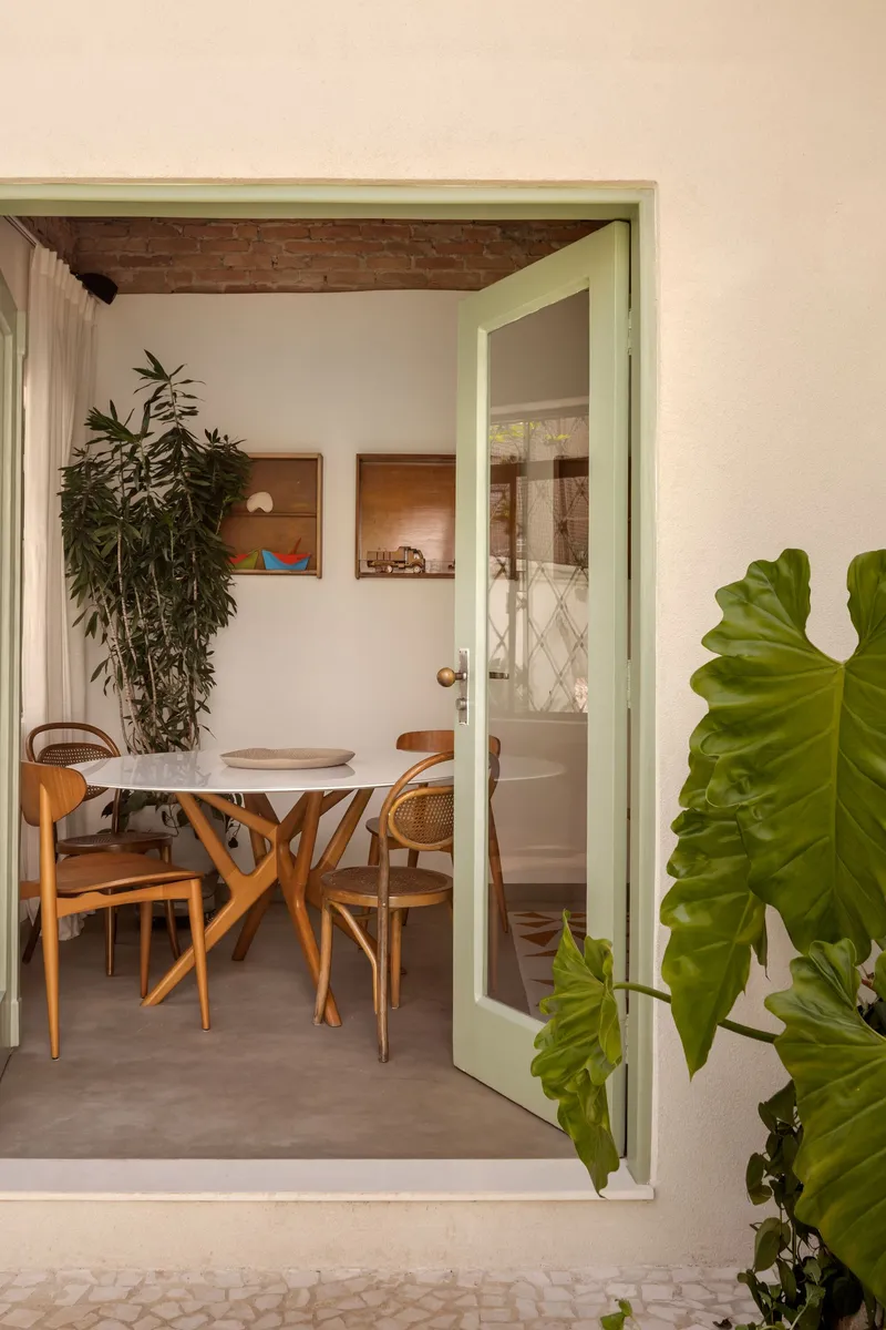 Pale green door frame opening to dining area with exposed brick ceiling and large tropical plants
