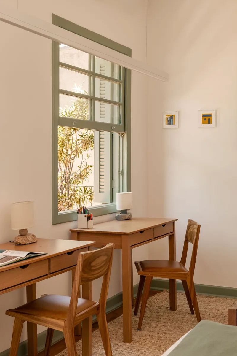 Study corner with wooden desks and chairs beneath tall window framing bamboo foliage outside