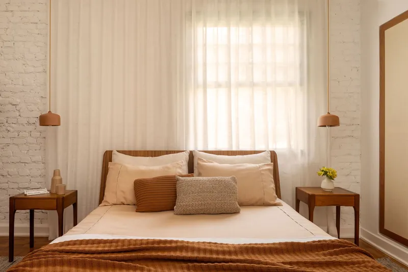 Bedroom with white brick wall, wooden bed frame and sheer curtains filtering afternoon light