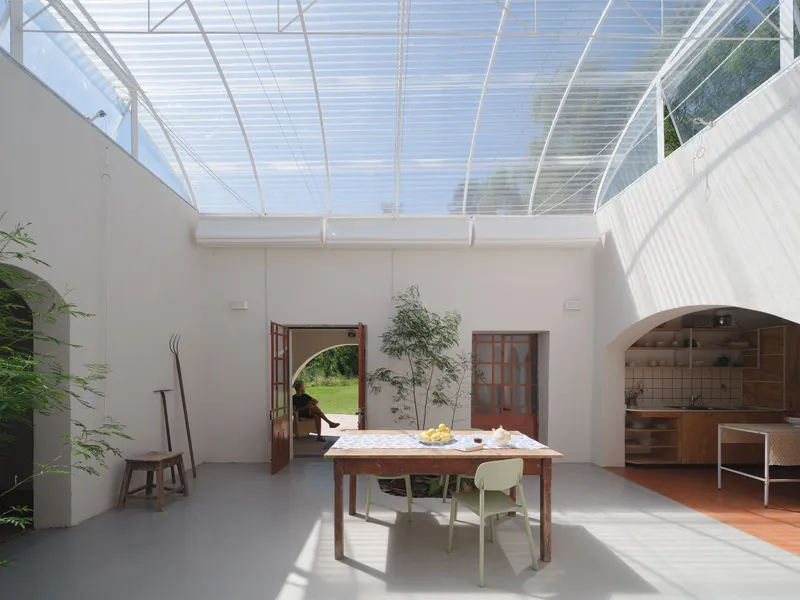 Interior courtyard with translucent arched roof, dining table and planted beds on polished concrete floor