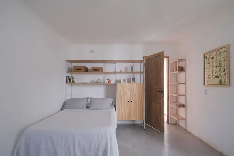 Bedroom with concrete floor, timber cabinetry and light shelving framing the bed