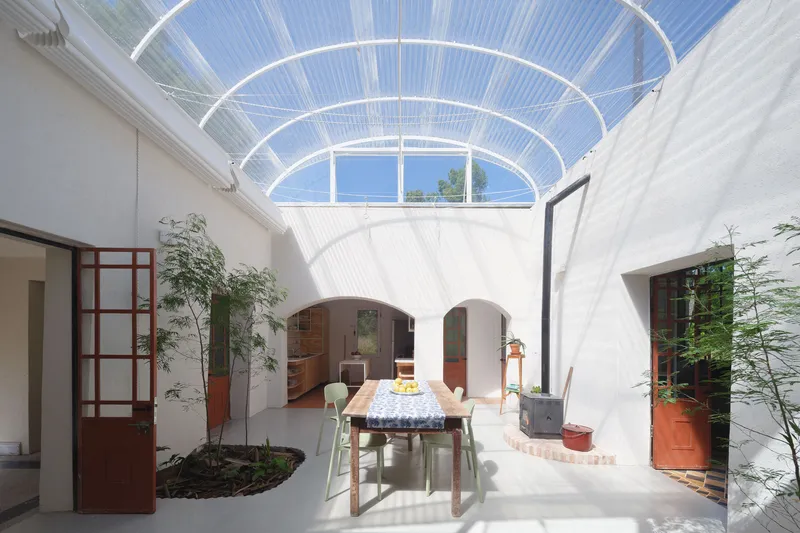 Courtyard with arched openings and translucent corrugated roof flooding white walls with dappled midday light