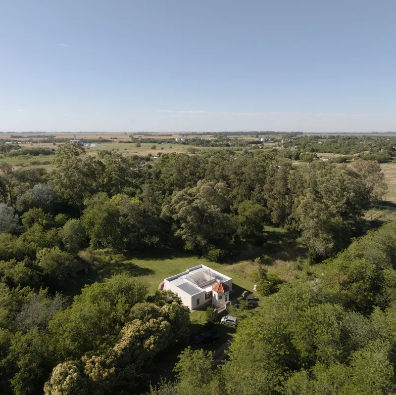 Drone perspective showing the building nestled among trees with open farmland beyond