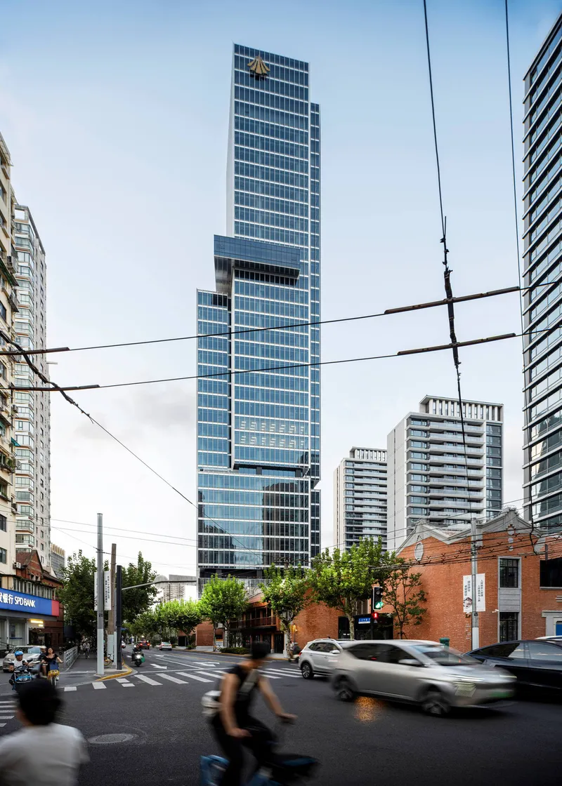 Vertical glass facade viewed from the street intersection with overhead wires and blurred pedestrians crossing