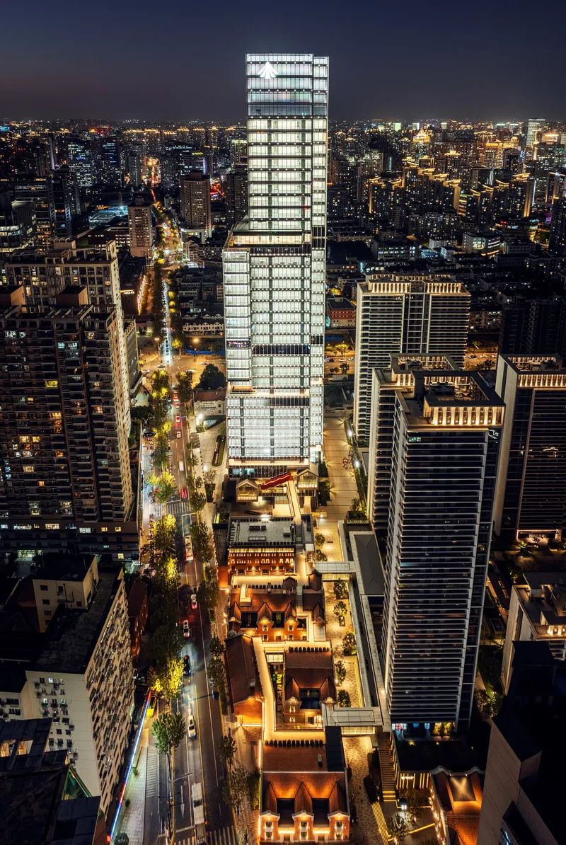 Aerial night view of the illuminated glass tower rising above surrounding buildings and streets