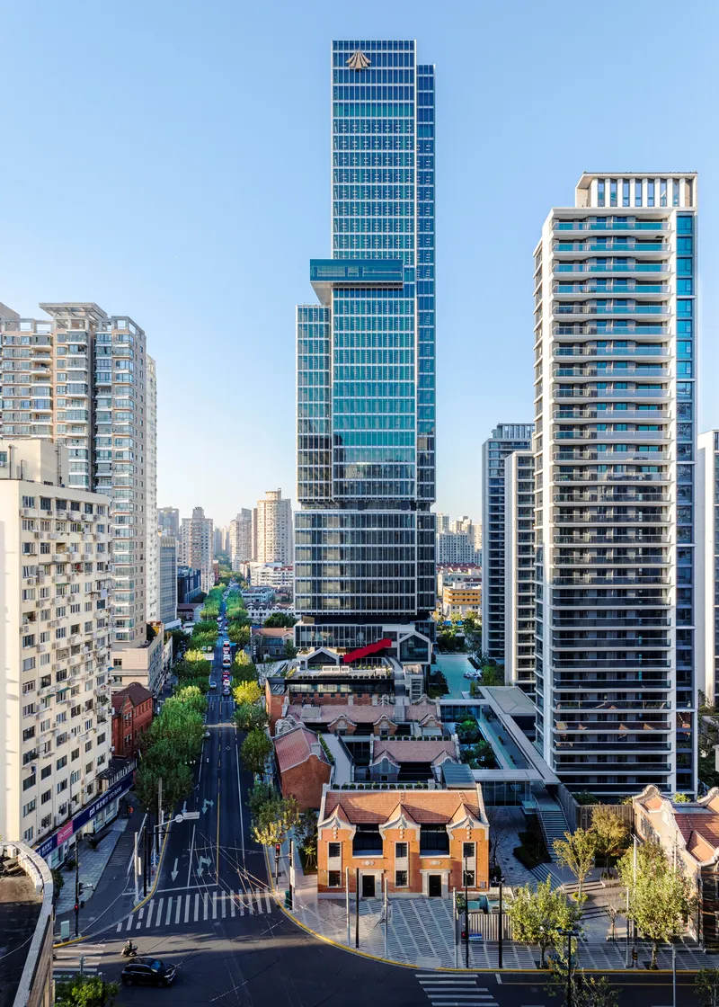 Glass curtain wall tower rising above tree-lined street and preserved brick heritage buildings