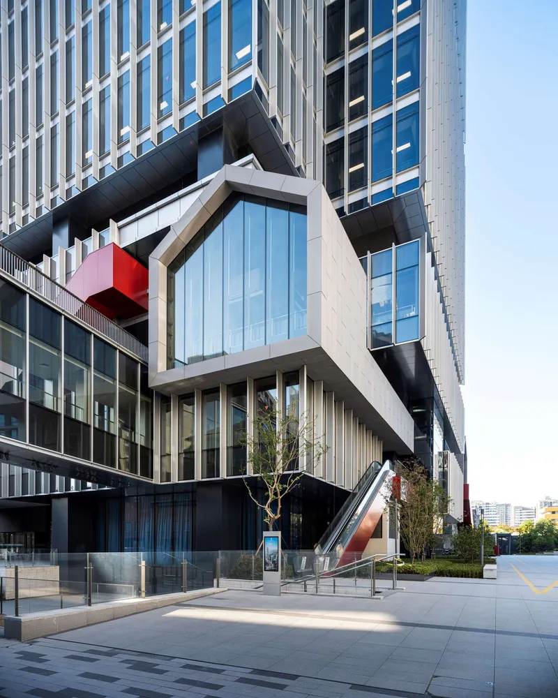 White cantilevered volume with pentagonal window and red sculptural element above ground-level plaza