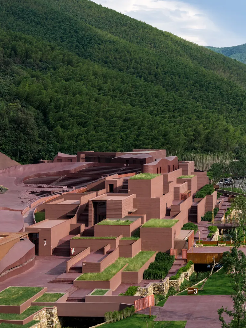 Stepped terraces and rooftop gardens descending the hillside backed by dense forest