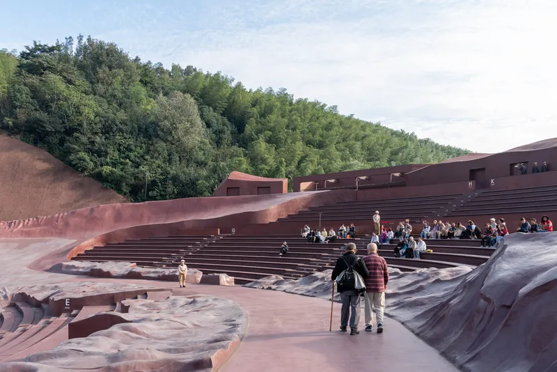 Visitors seated in the amphitheatre bowl with terraced red stone seating facing the wooded slope