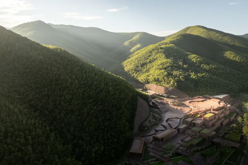 Aerial view of the complex nestled into a valley with surrounding forested mountains at dusk