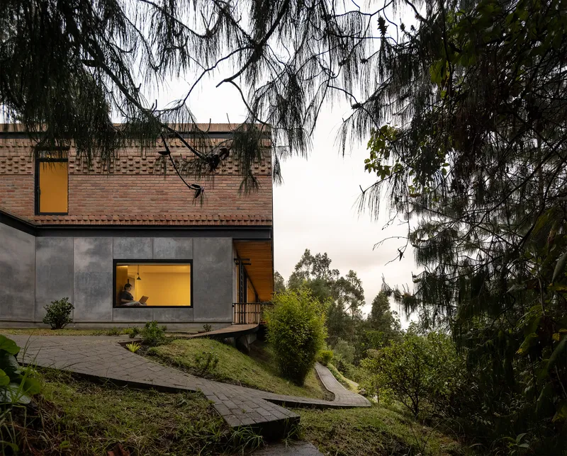 Concrete and brick facade with illuminated windows framed by overhanging willow branches at twilight