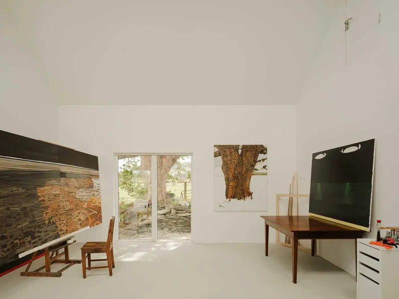 White-walled studio space with glazed doors opening to a stone wall and sunlit garden beyond
