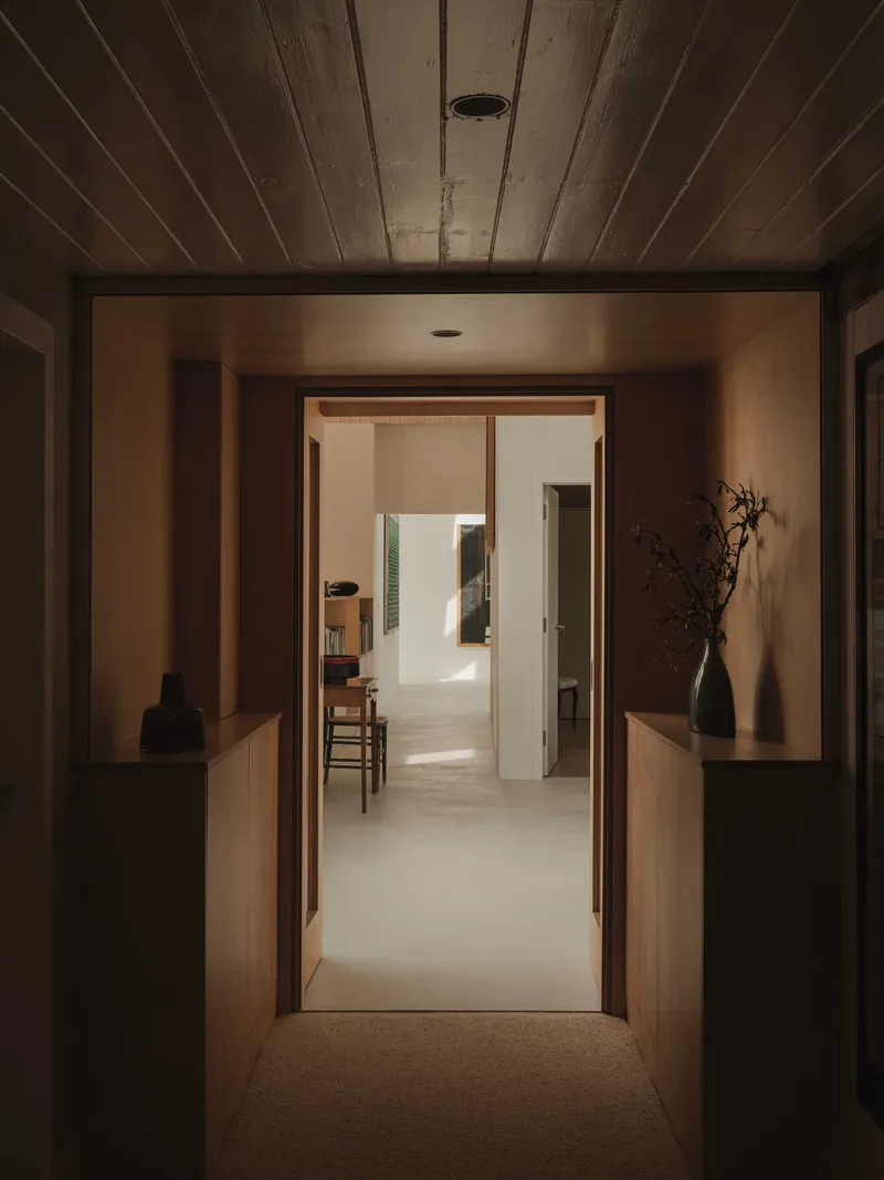 View through timber-framed doorway with wood plank ceiling leading to sunlit rooms beyond