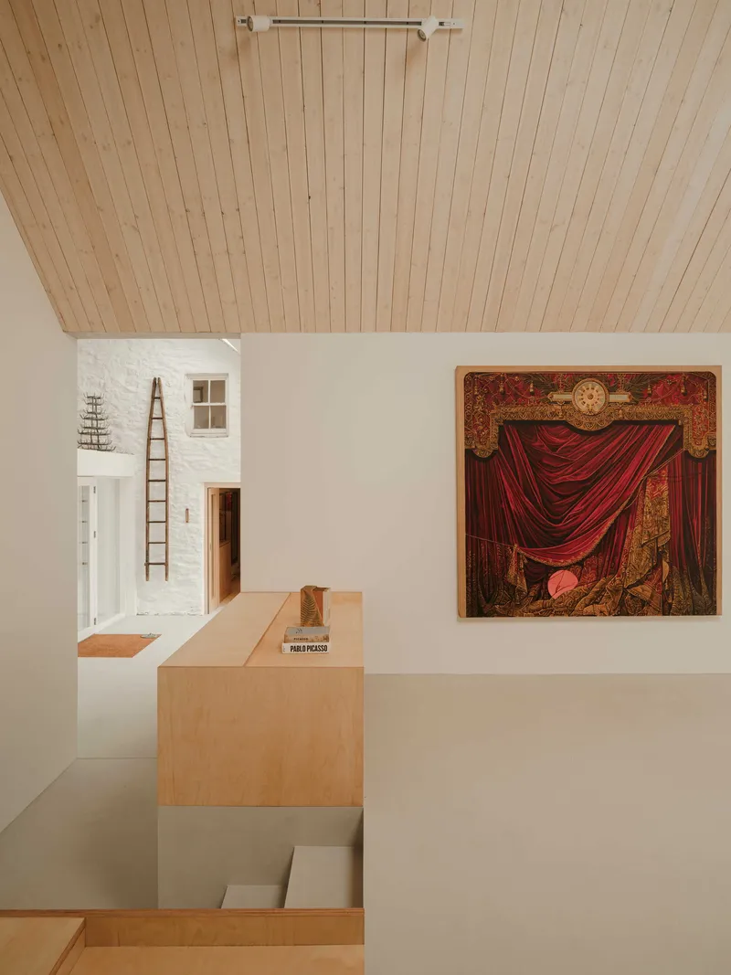 Interior view of a timber-lined vaulted ceiling above white walls displaying a red curtain painting