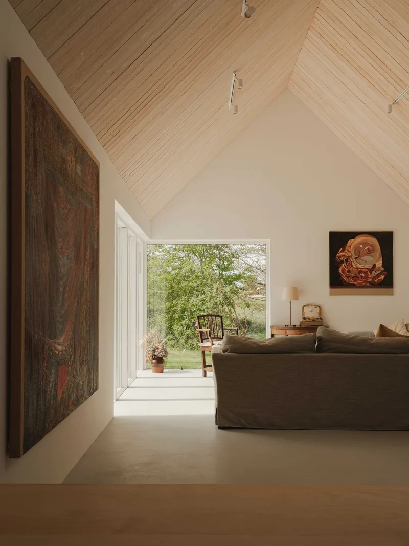 Living space with vaulted timber ceiling and full-height window framing a view of green trees outside