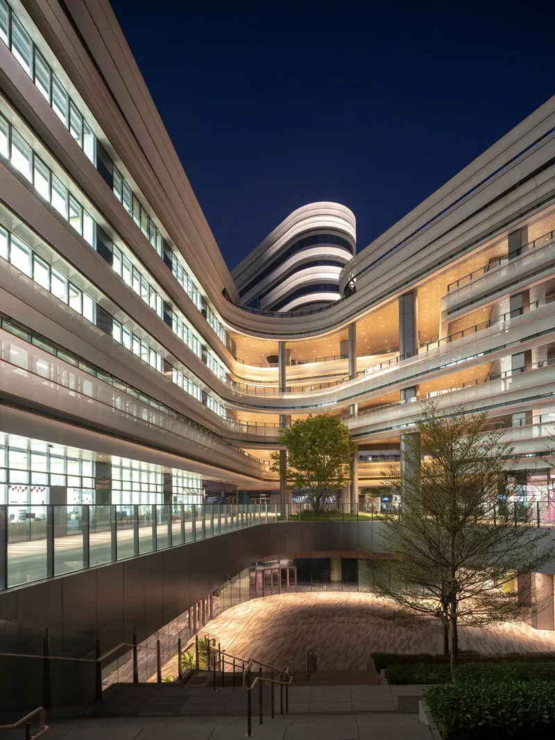 Courtyard view at night showing illuminated terraces, planted tree and curved tower rising above