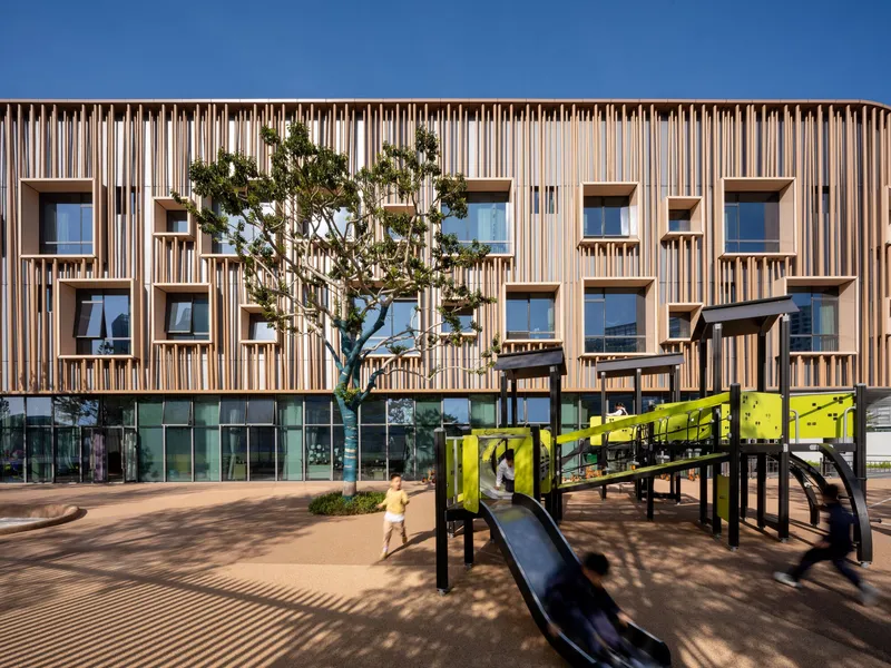 Timber screen facade with planted tree and yellow playground equipment in the foreground