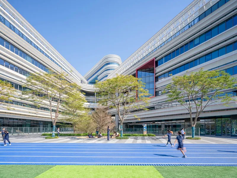 Courtyard with blue running track and people walking among trees framed by horizontally striped glass facade volumes