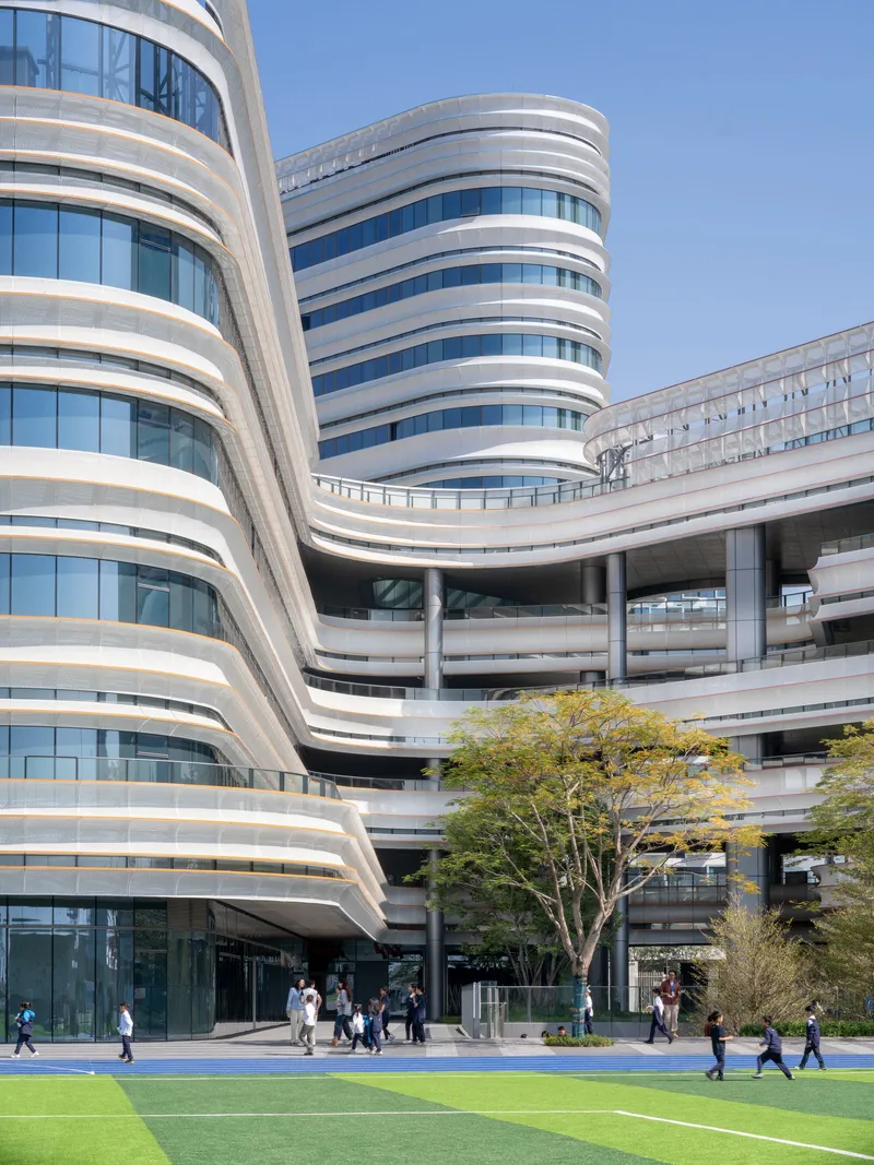 Ground-level view of curved facade towers with alternating white bands and glazing above blue track and green lawn