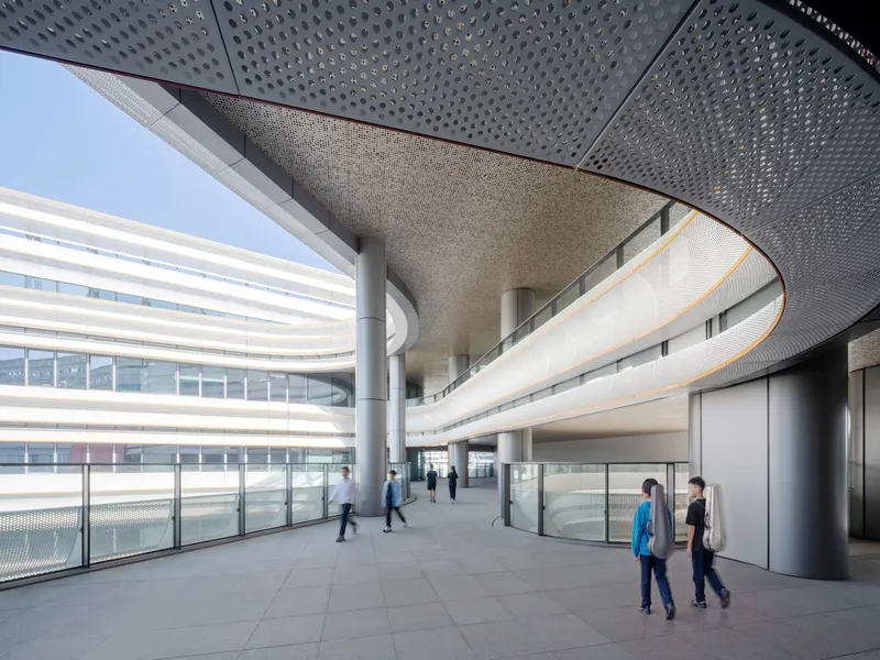 Interior corridor with perforated ceiling panels and curved balconies overlooking the ground floor circulation space