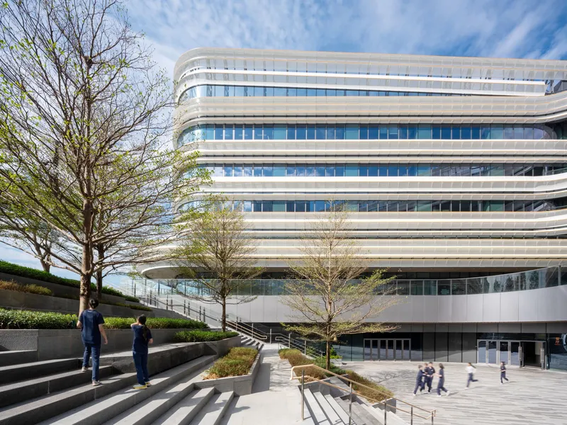 Terraced landscape with concrete steps, planted beds, and spring trees beside the horizontally banded glass facade