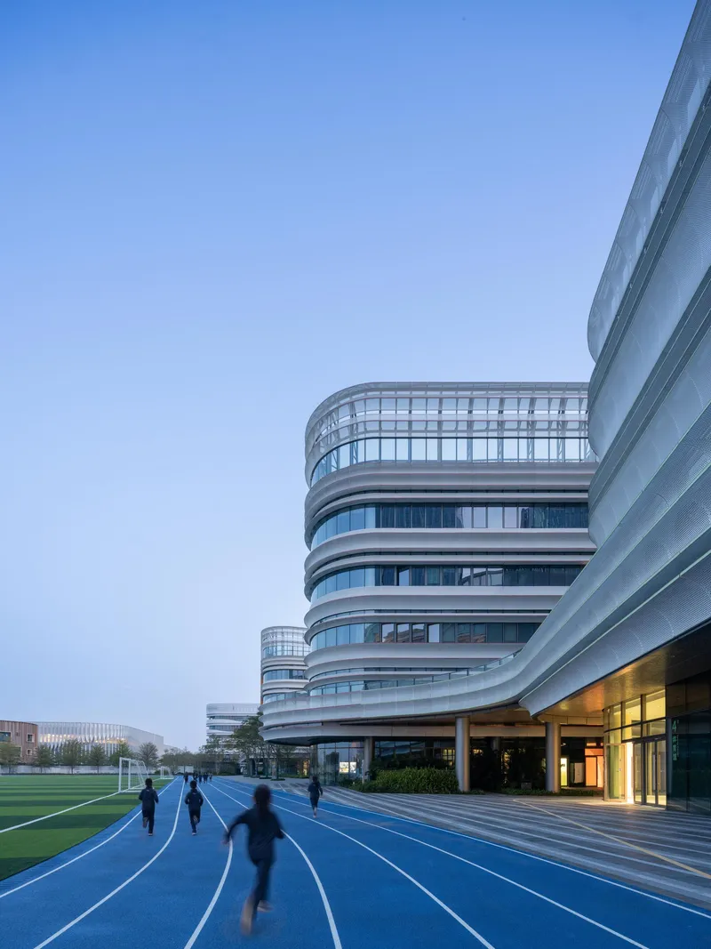 Blue running track curving past the ground floor entrance with figures jogging at dusk