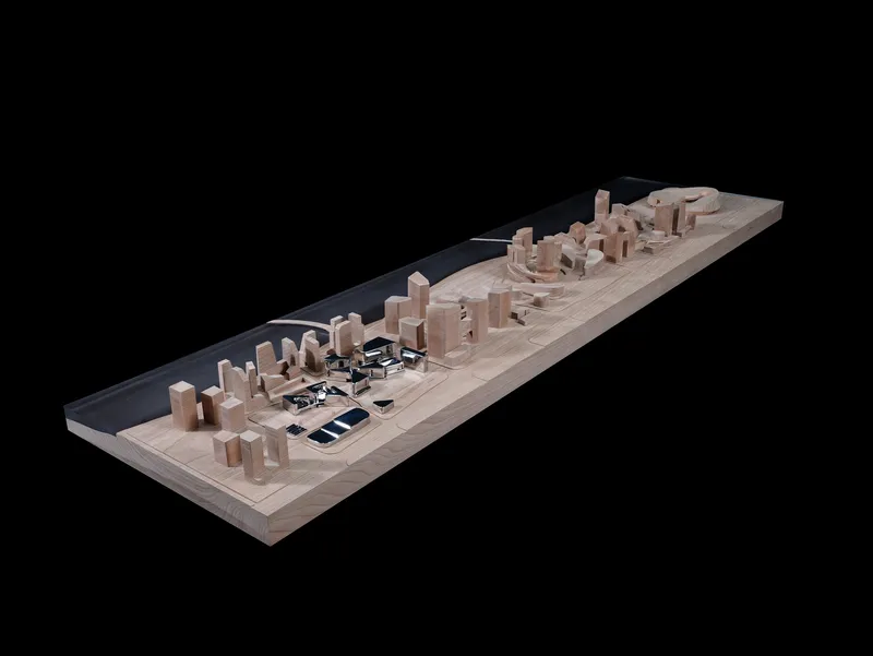 Physical model showing a linear urban development along a waterfront with varied building volumes in timber and black