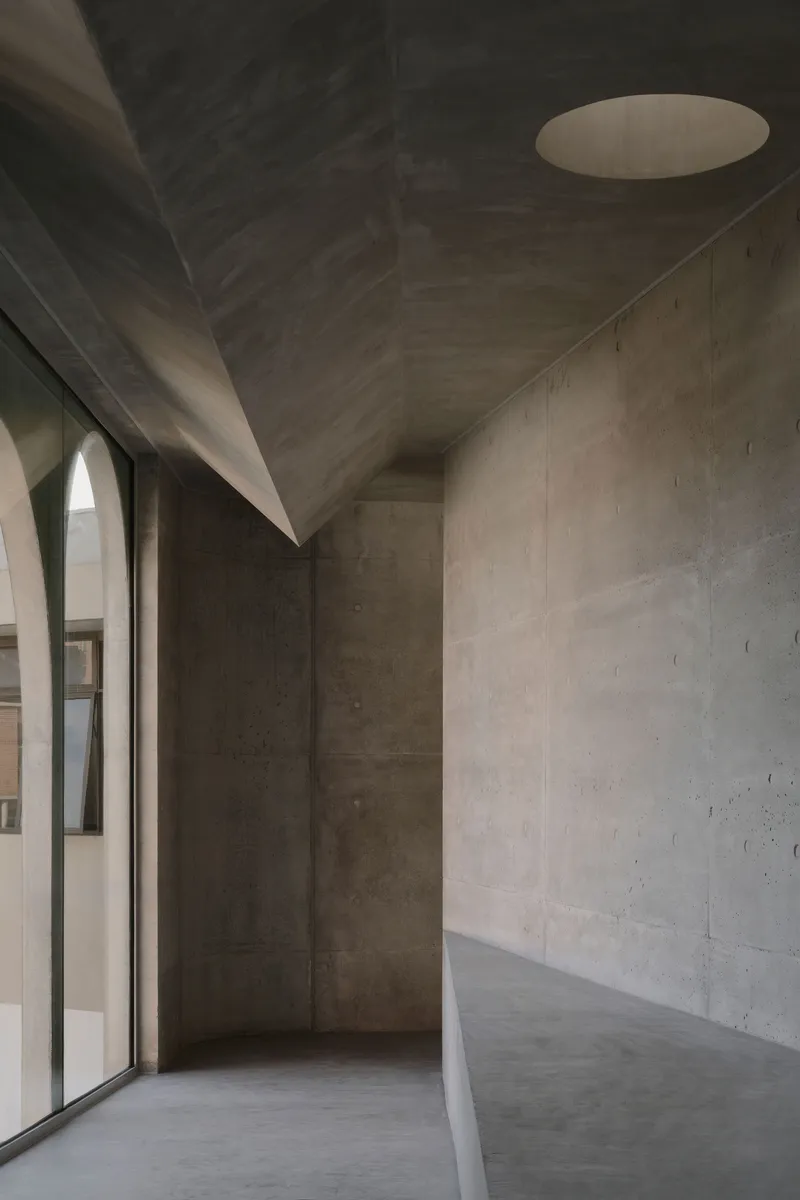 Board-formed concrete interior space with folded ceiling planes and a circular skylight