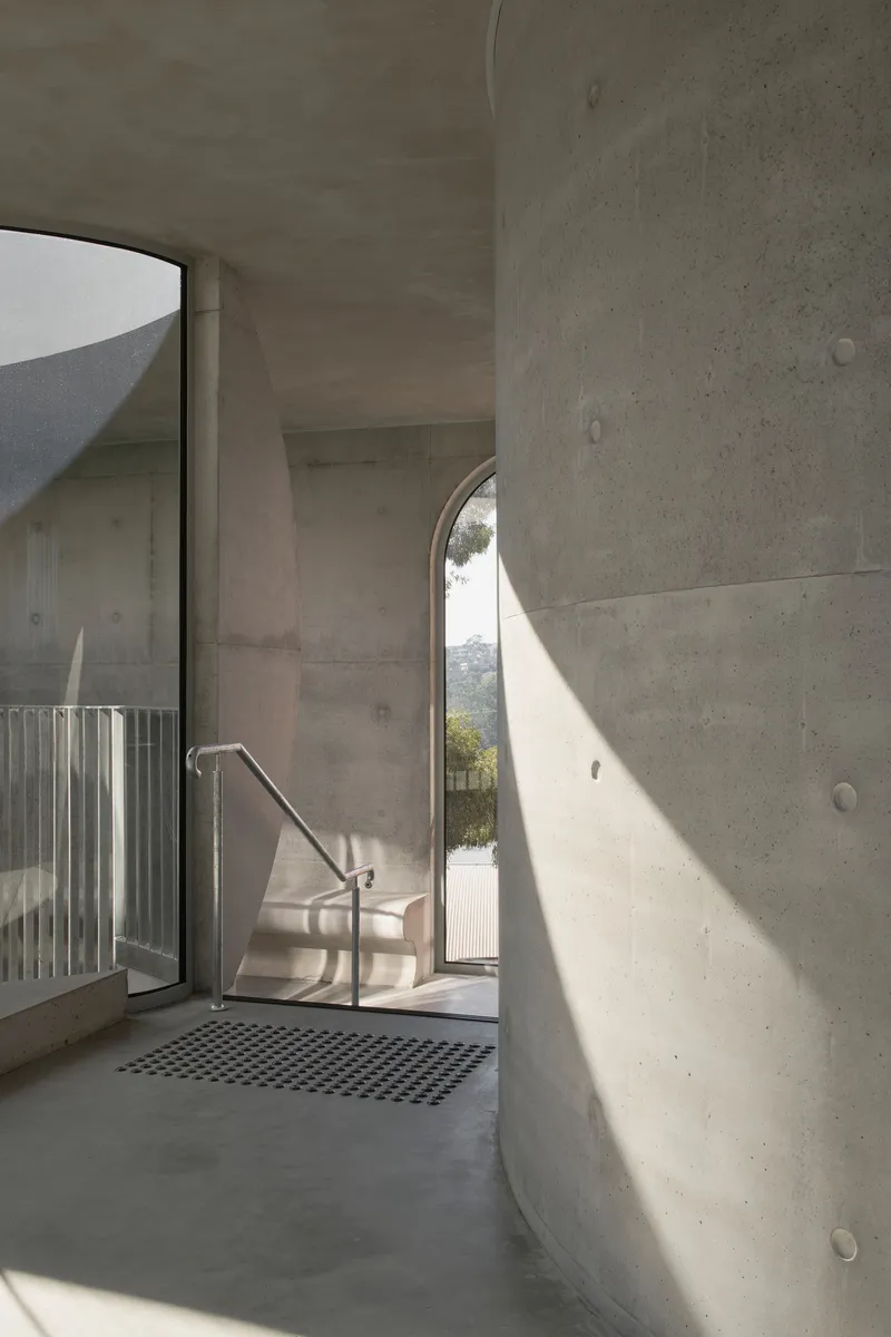 Concrete interior with arched doorway casting sunlight onto the walls and metal grate floor