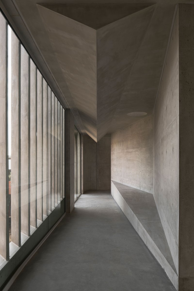 Concrete corridor with vertical louvered glazing filtering natural light along one side