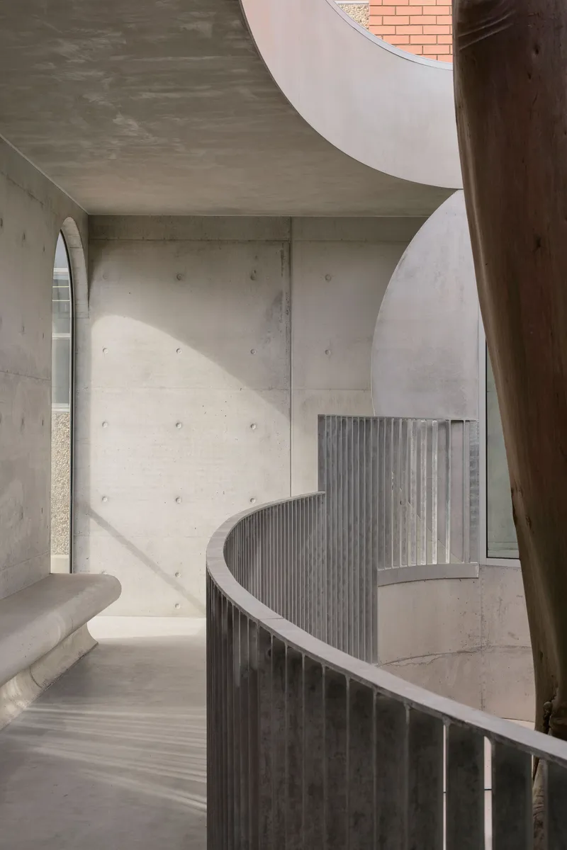 Helical concrete staircase with vertical balustrade wrapping around a timber column in daylight