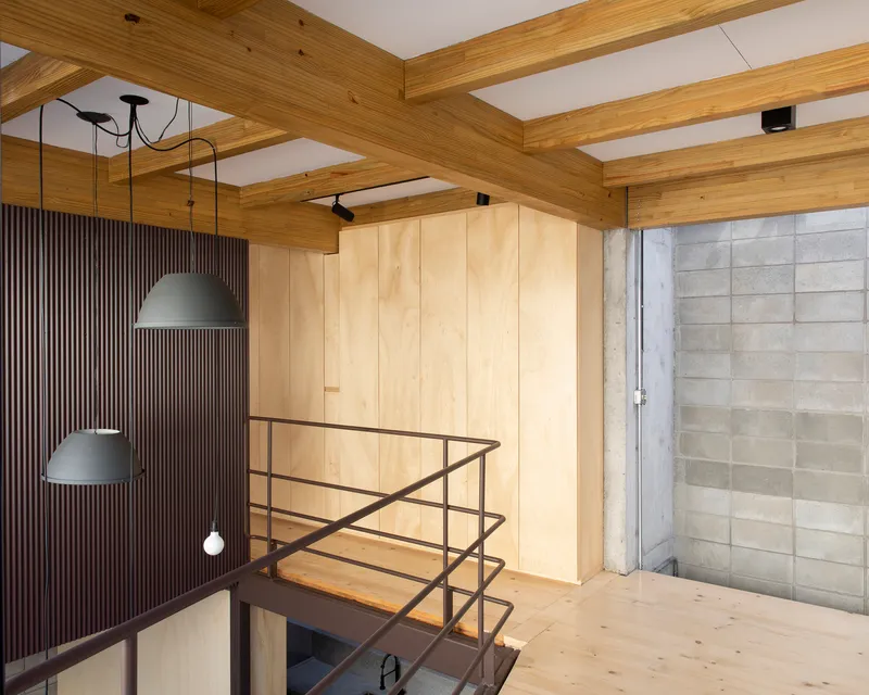 Upper level passage with plywood storage volume and steel railing overlooking lower space