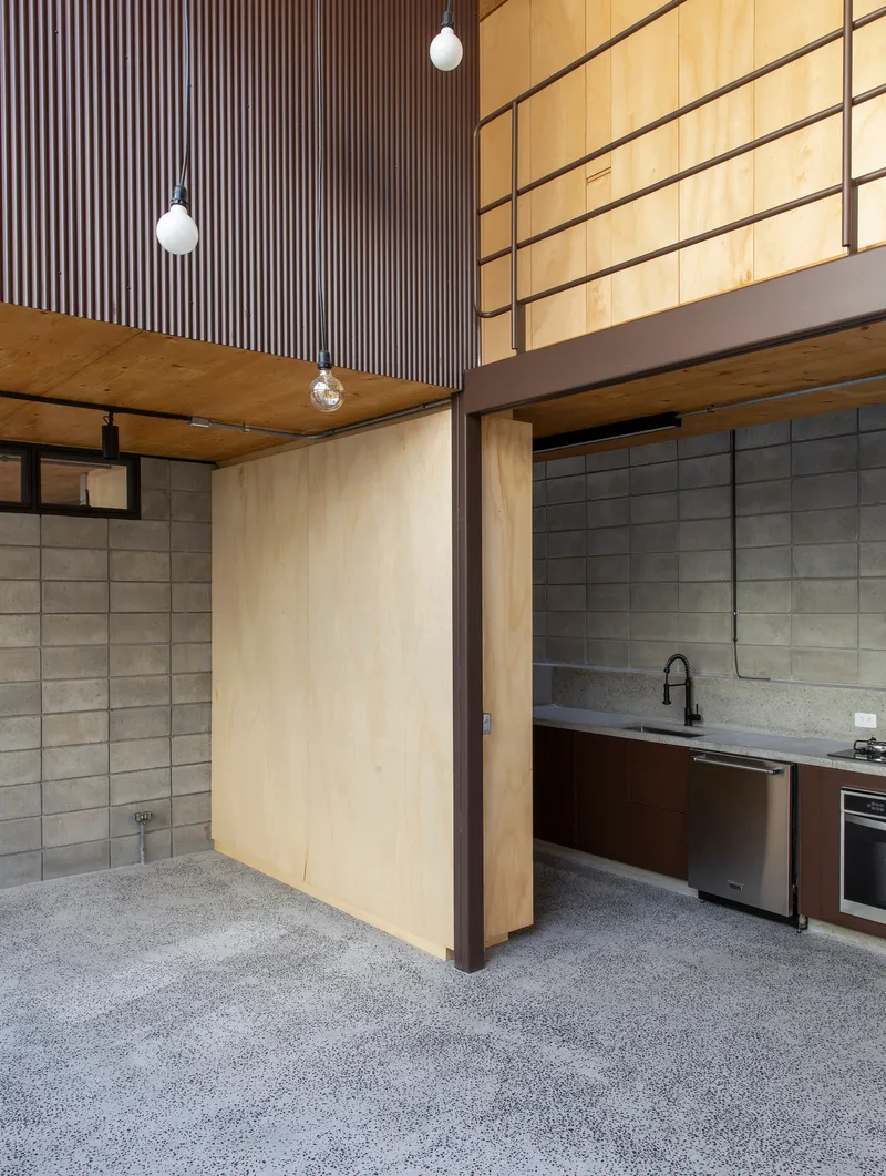Kitchen counter with concrete block walls, plywood cabinetry and mezzanine guardrail under pendant lighting