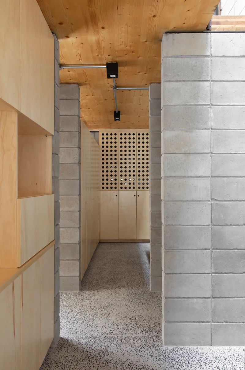 Corridor view through concrete block walls toward plywood storage with perforated door panel