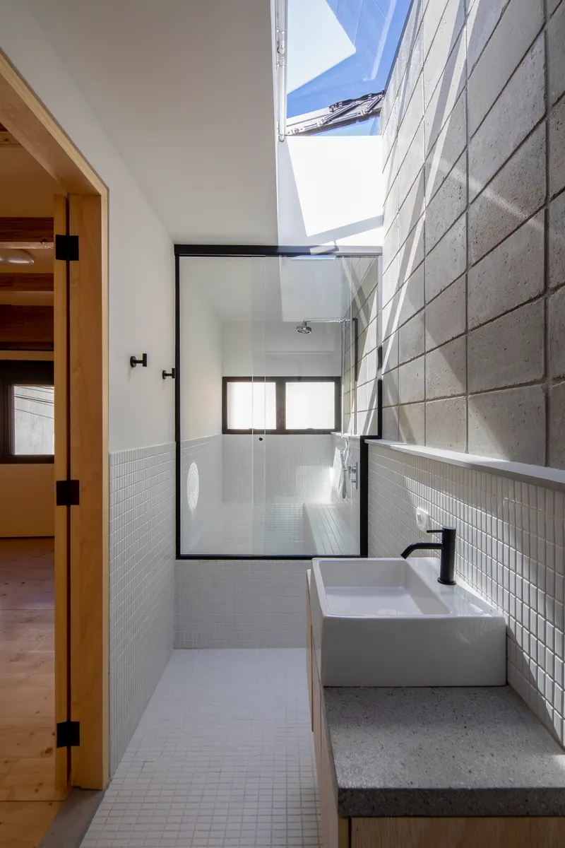 Bathroom with white mosaic tile walls, glass shower enclosure, concrete basin counter and overhead skylight