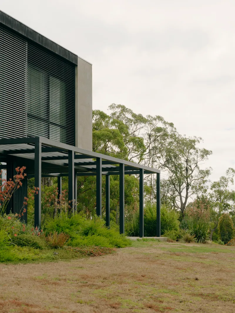 Elevated pavilion with steel column grid and horizontal louvres above a planted slope in overcast weather