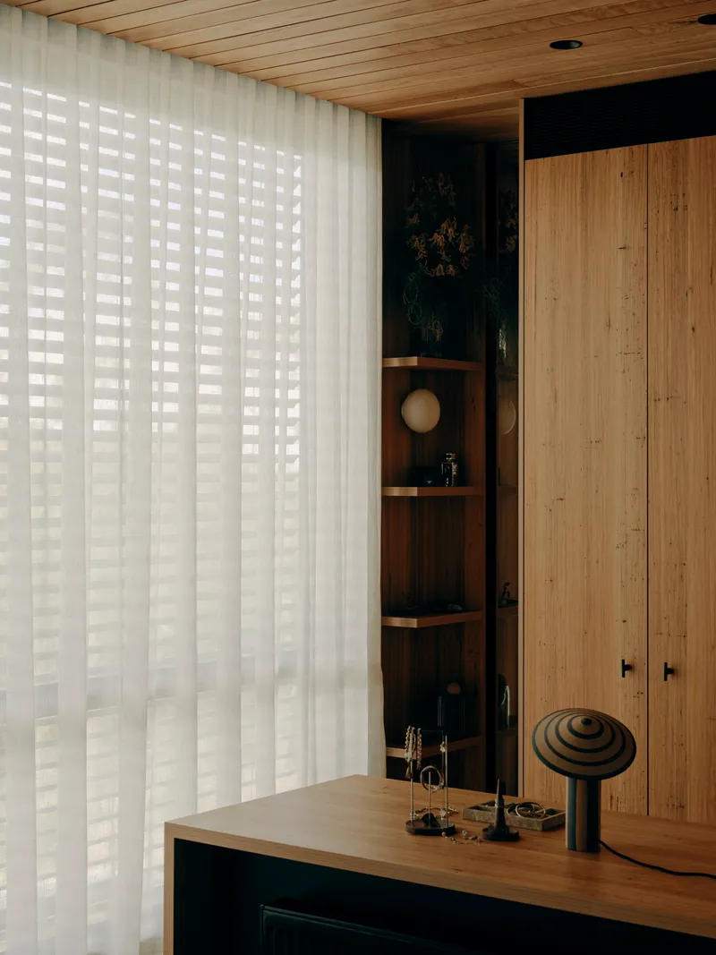 Timber desk with sculptural objects against backlit vertical blinds and a recessed display niche