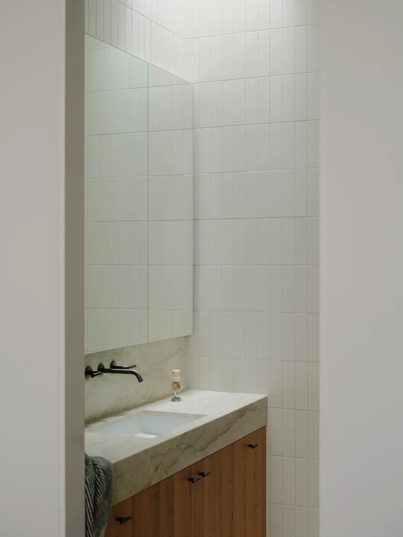 Bathroom vanity with stone countertop and timber cabinetry framed by large-format white tile walls