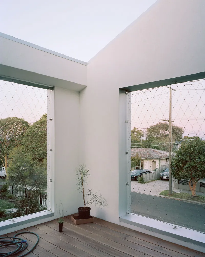 Corner balcony with timber decking and mesh safety screens framing views to the street