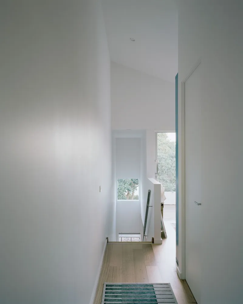 Narrow corridor with light wood flooring and a striped blue rug leading to a window with garden view