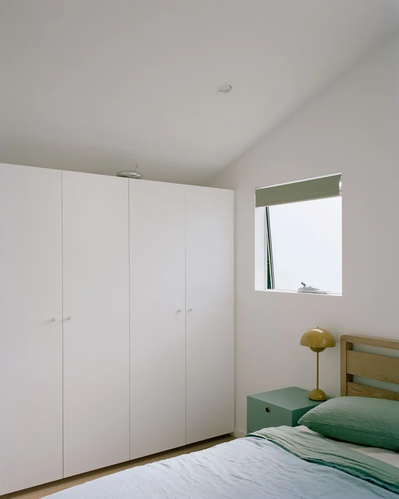 Bedroom with white built-in wardrobes and a square window framing natural light above the bedside table