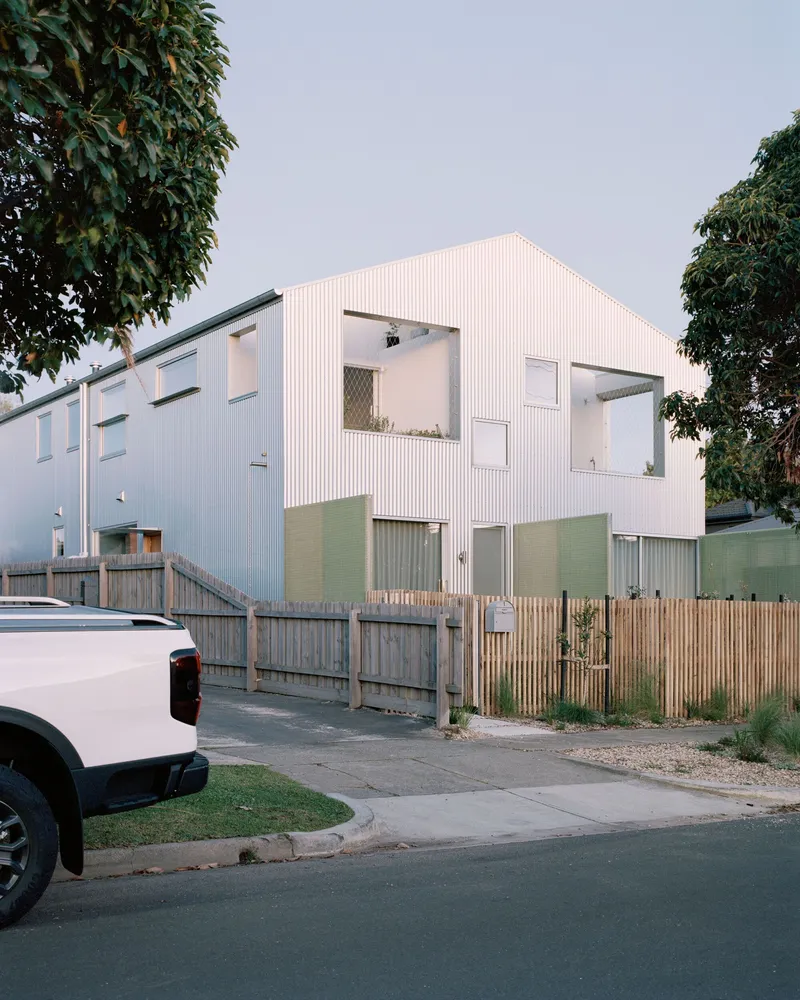 Street view of the white corrugated metal facade with timber fencing and foliage at dusk