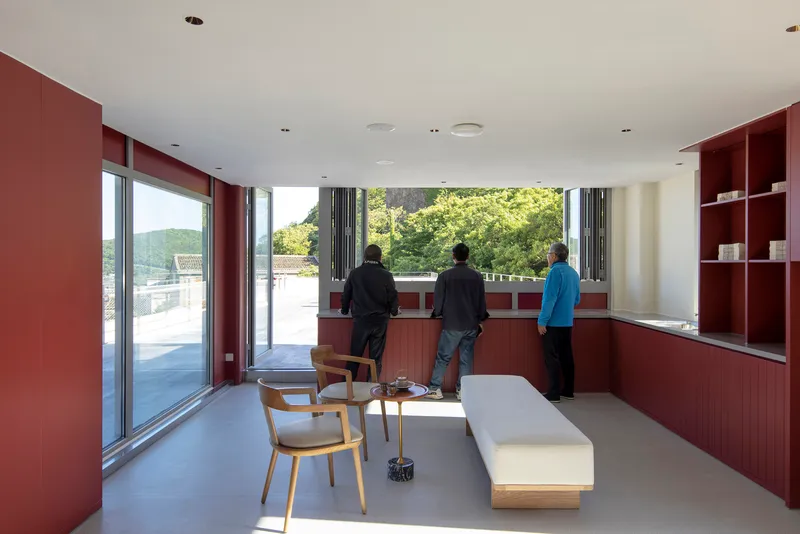 Living room with red built-in millwork and three people looking out toward treetops in daylight