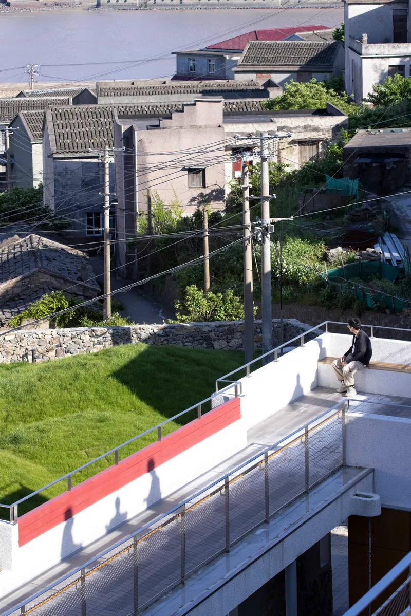 Rooftop terrace with grass lawn and metal railing overlooking neighboring rooftops and utility poles