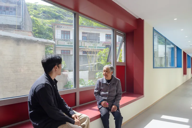 Red window alcove with built-in bench seating where two people sit in conversation