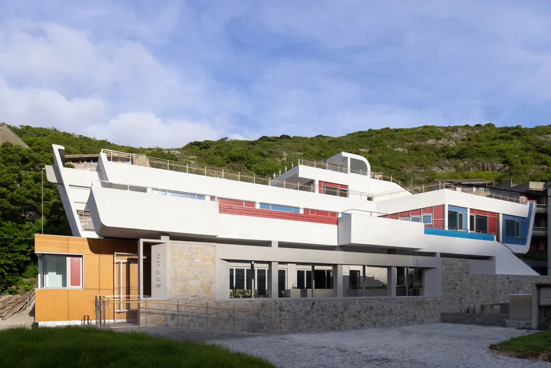 White rendered facade with stone plinth and colored window panels set against a forested hillside