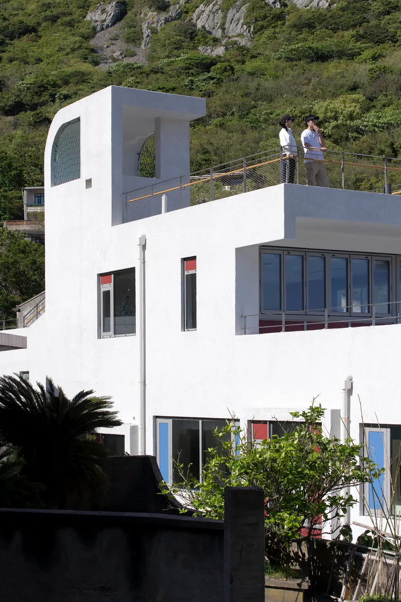 White rooftop terrace with curved tower element and two figures standing by the mesh railing
