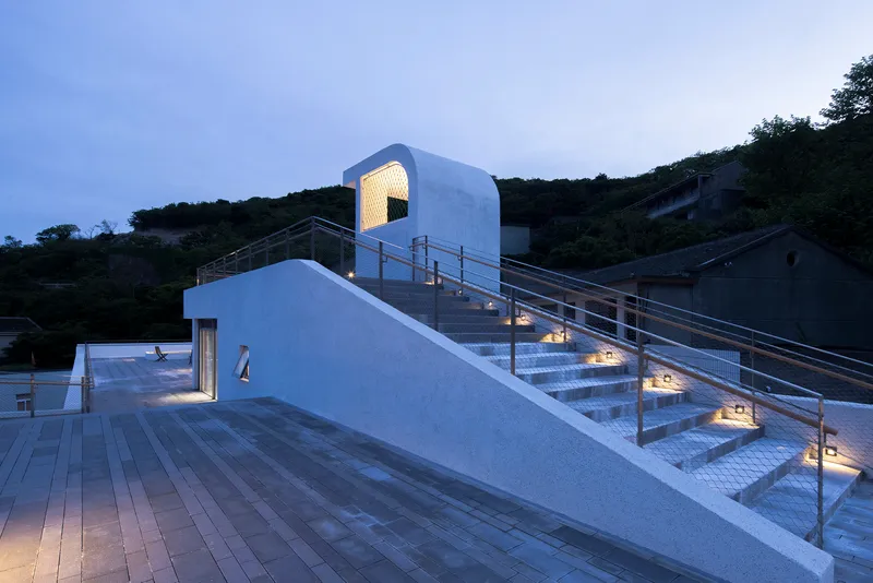 Illuminated staircase with metal railings ascending from a timber deck at dusk