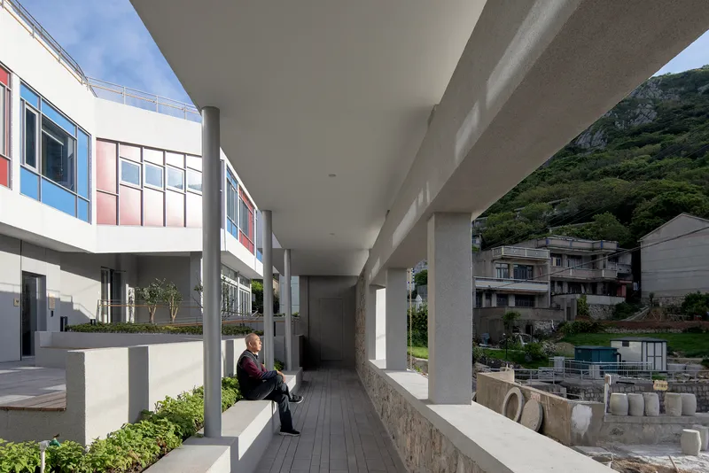 Covered corridor with concrete columns and planted beds where a person sits reading